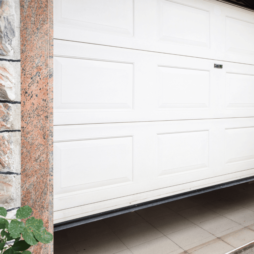 White garage door with raised panels and stone exterior showing weather seal at bottom